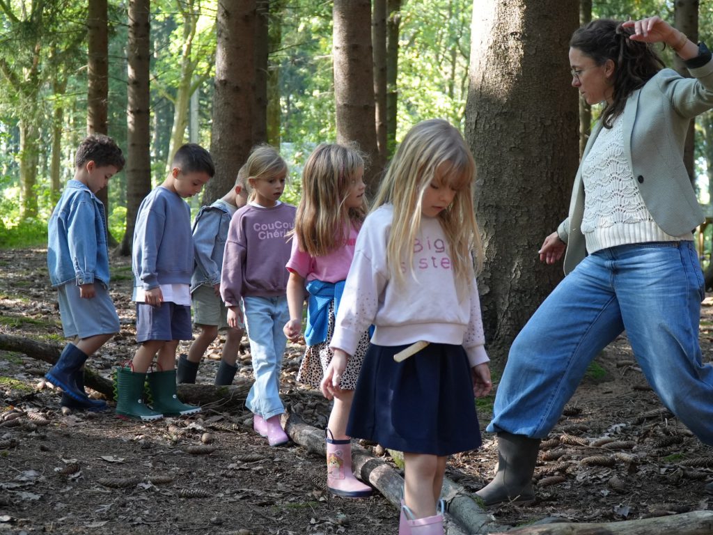 Une enseignante accompagne les élèves sur un parcours de troncs dans le bois