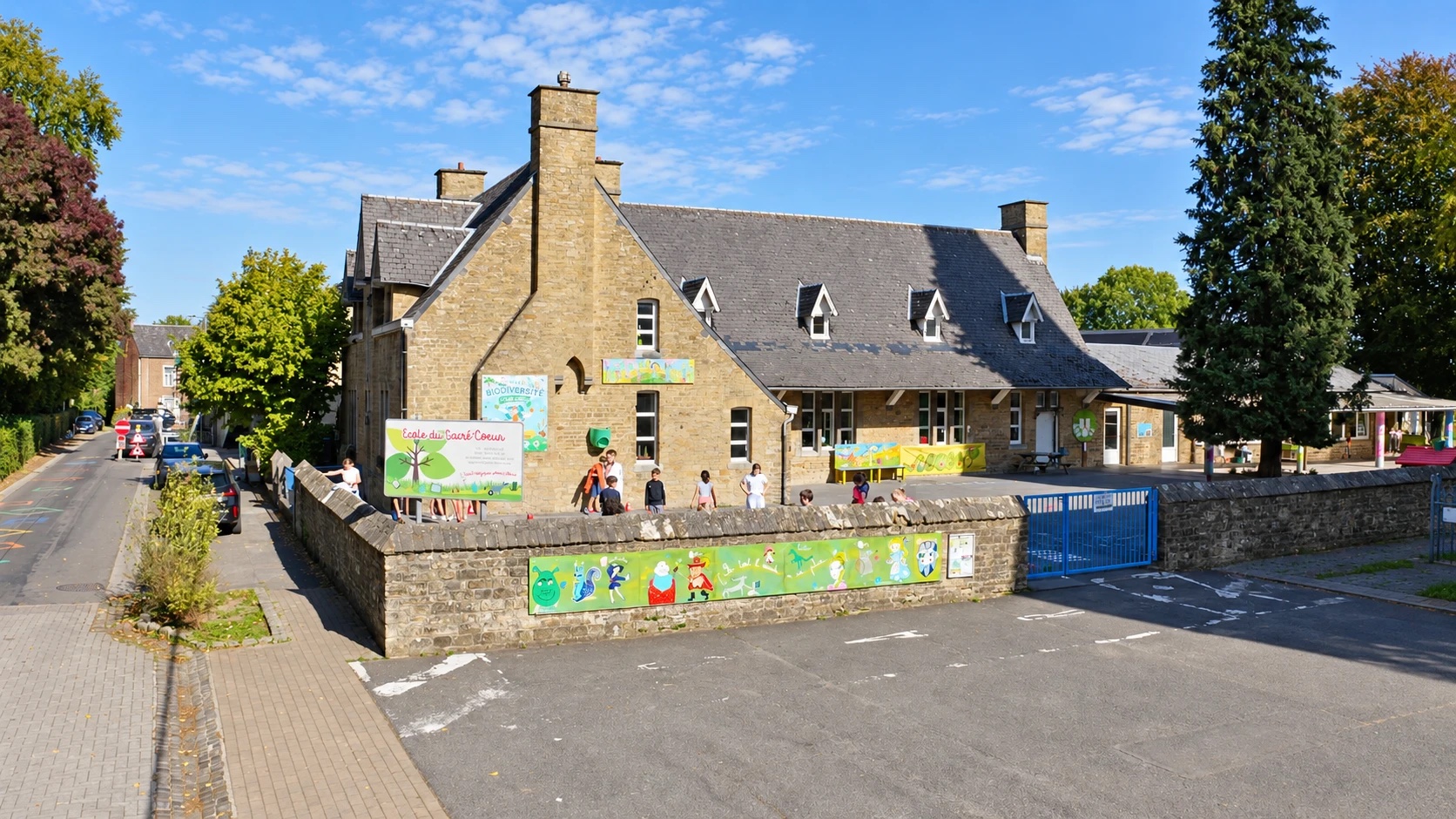 La façade en pierre de l'école du Sacré-Cœur et sa cour de récréation, un jour de soleil